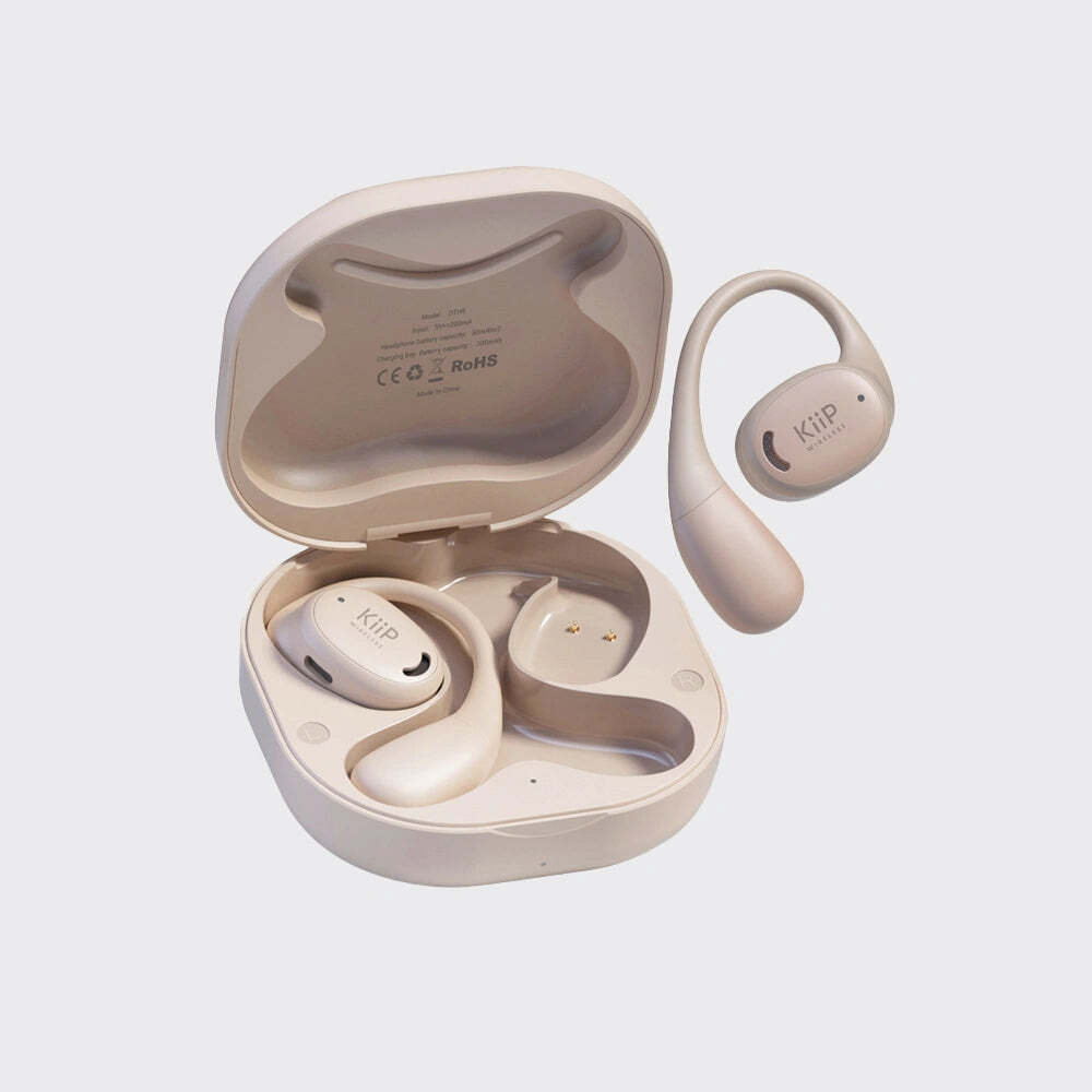 A pair of beige wireless earbuds with an open matching charging case on a light gray background. The earbuds have a small smiley face logo on the front, and the inside lid of the case shows regulatory text.