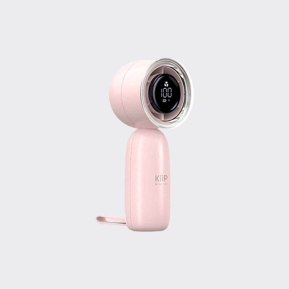 A light pink handheld fan with a circular digital display on the front and a wrist strap, shown against a solid light gray background.